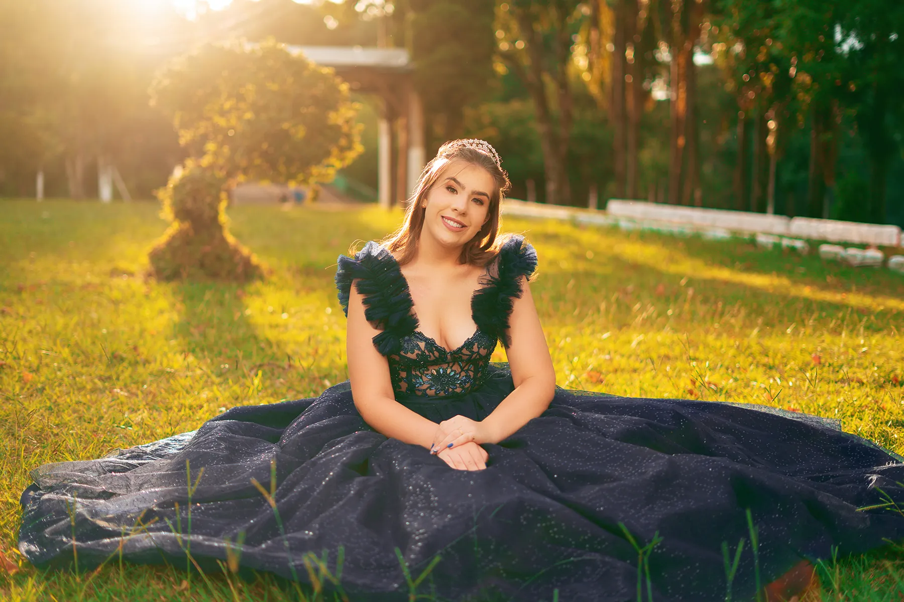 Debutante sentada no gramado com o vestido aberto ao redor, ao pôr do sol